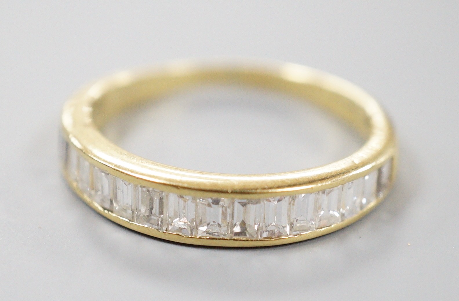 A modern 18ct gold and graduated baguette cut diamond set half eternity ring, size Q, gross 3.4 grams.